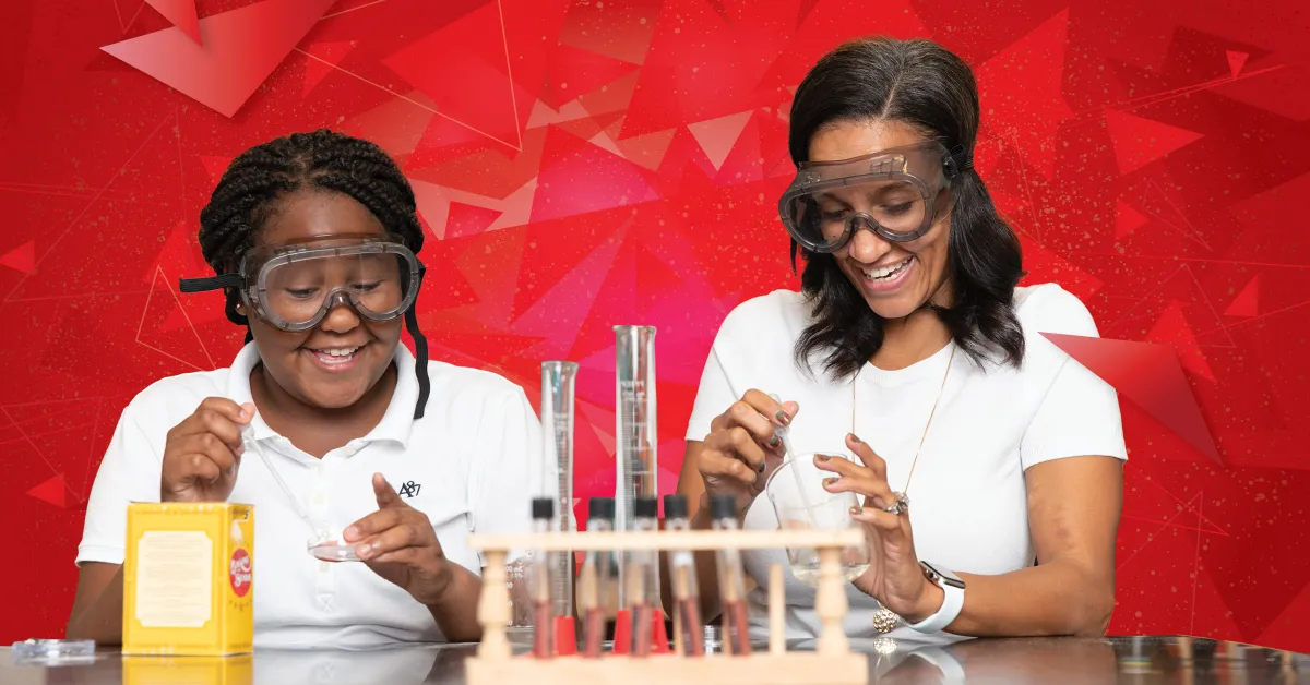 A smiling student and an adult mentor wearing safety goggles perform a science experiment together. They are handling glass beakers and test tubes at a lab table, with a bright red geometric background behind them. Both appear engaged and enthusiastic.